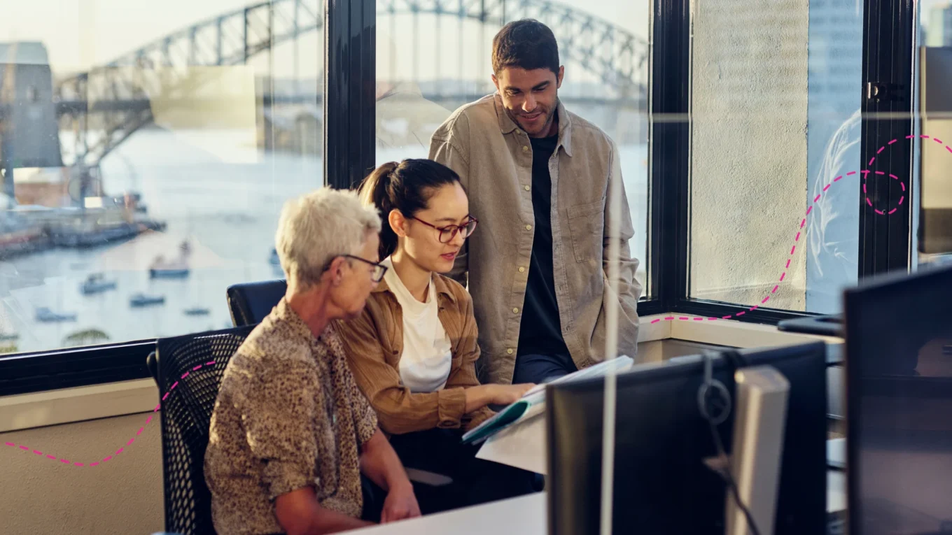 Three people looking at a computer together in an office with Sydney Harbour bridge in the background