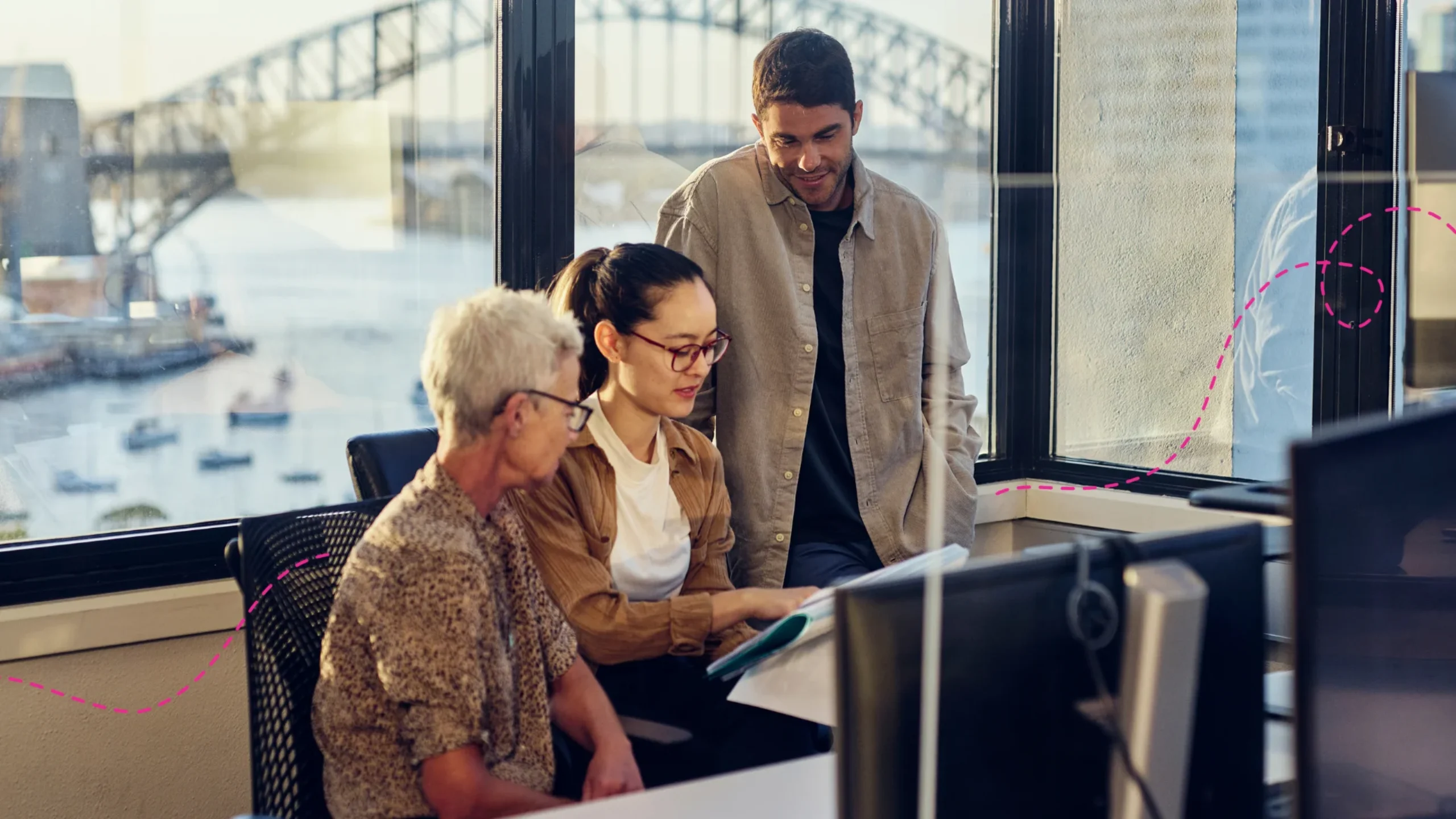 Three people looking at a computer together in an office with Sydney Harbour bridge in the background