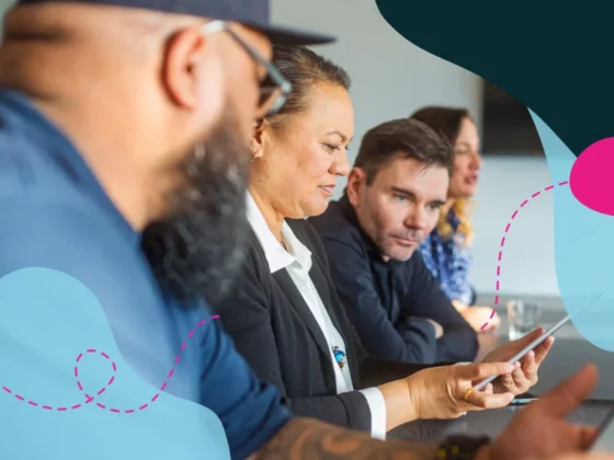 People sat at a boardroom desk in a meeting looking at a tablet