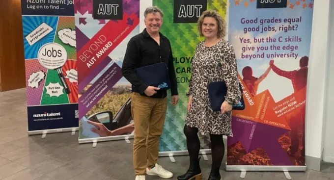 Two smiling professionals holding Salt folders, standing in front of AUT career and awards banners.