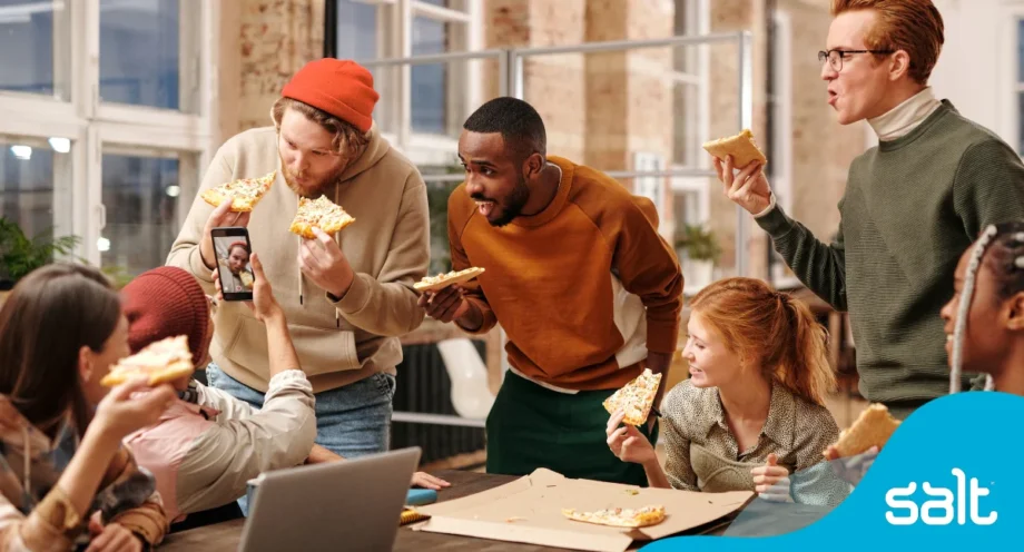 Team of people cheering with slices of pizza looking happy in an office setting