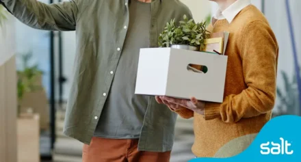 A new employee with a box of personal belongings being introduced to the workspace, representing the first day at work