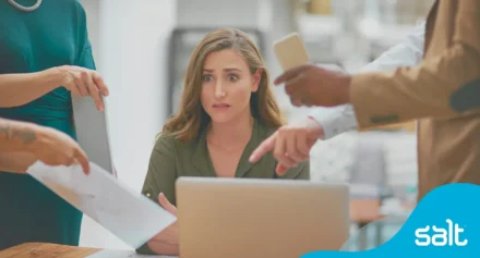 Woman looking anxious sat at her desk with too many people trying to speak to her at once