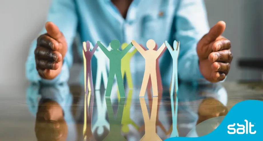 Close-up of a person's hands encircling a group of multicoloured paper cutout figures holding hands, symbolising protection, unity and diversity