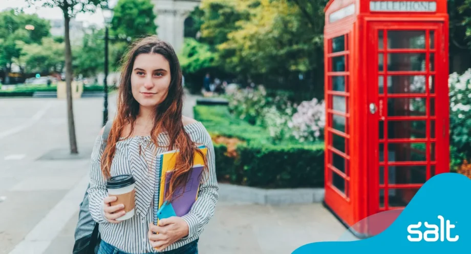 A woman holding books and a coffee cup stood beside a red telephone box