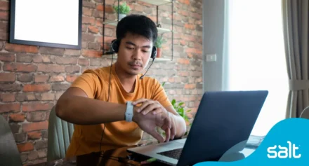 Man sitting at his home desk in front of his laptop looking at his watch