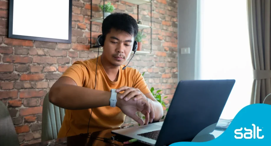 Man sitting at his home desk in front of his laptop looking at his watch