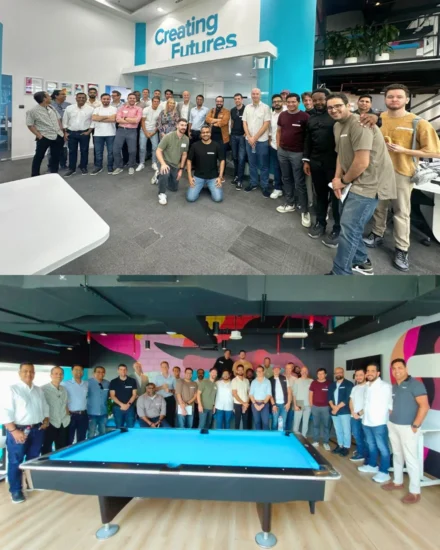 A large group of people posing together in an office environment and a recreational area with a pool table, smiling at an event