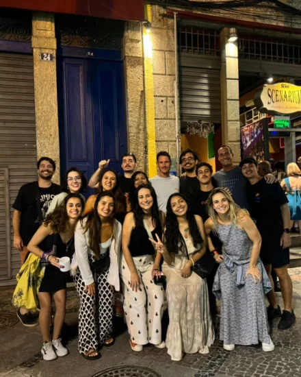 Group of coworkers smiling and posing together outside a venue at night during a year-end celebration in Rio de Janeiro
