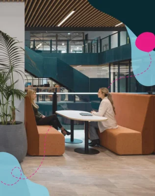 Two people sat at communal office space engaging in conversation