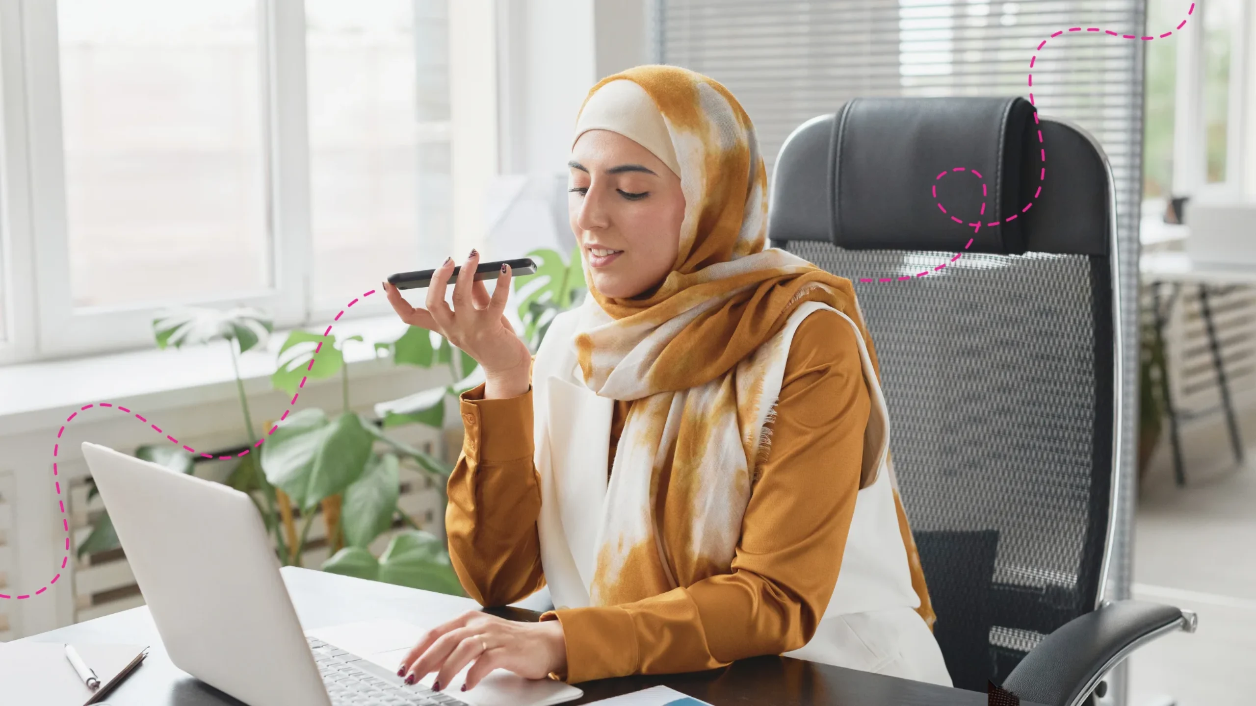 Emirate woman sitting at her desk on a call and working on her laptop